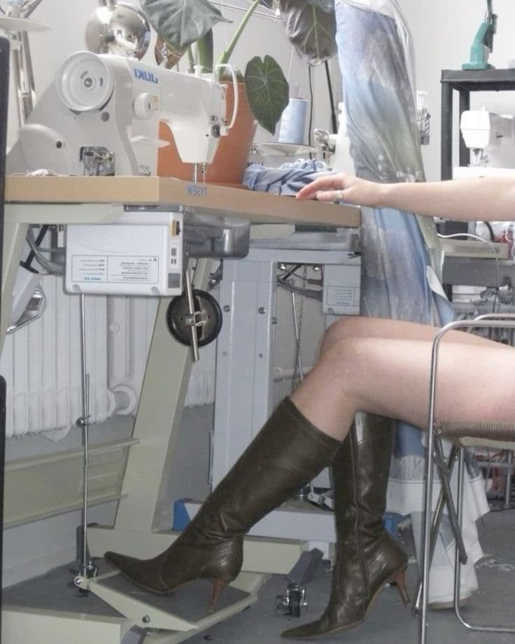 A machinist in knee-high boots at an industrial sewing machine