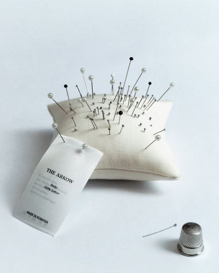 A cream pincushion studded with pearl-headed pins beside a thimble