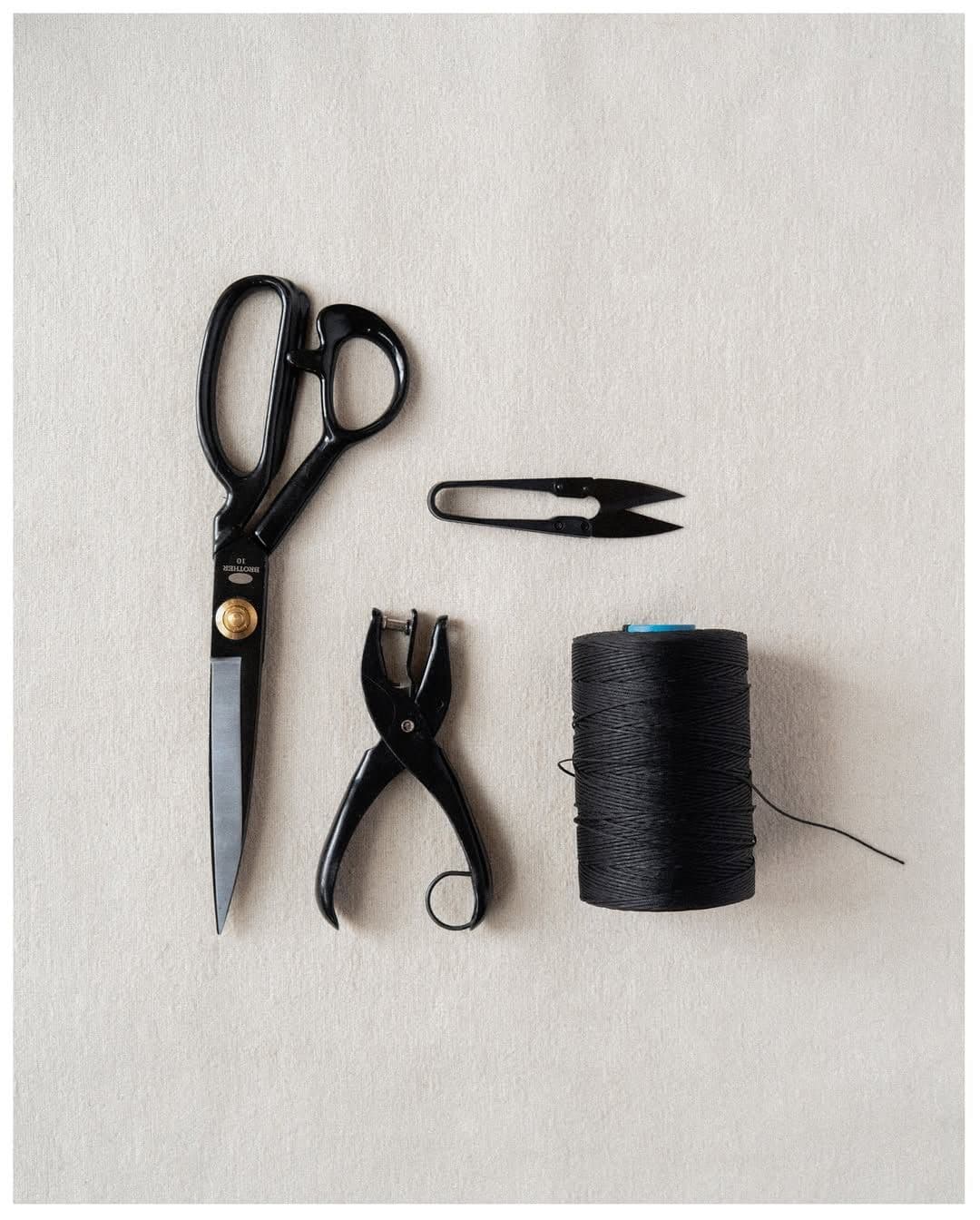 Tailor's shears, a hole punch, thread snips and a black thread spool on greige cloth
